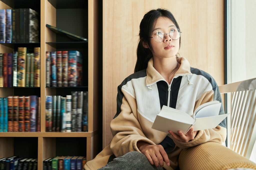 Young woman reads and daydreams near books.